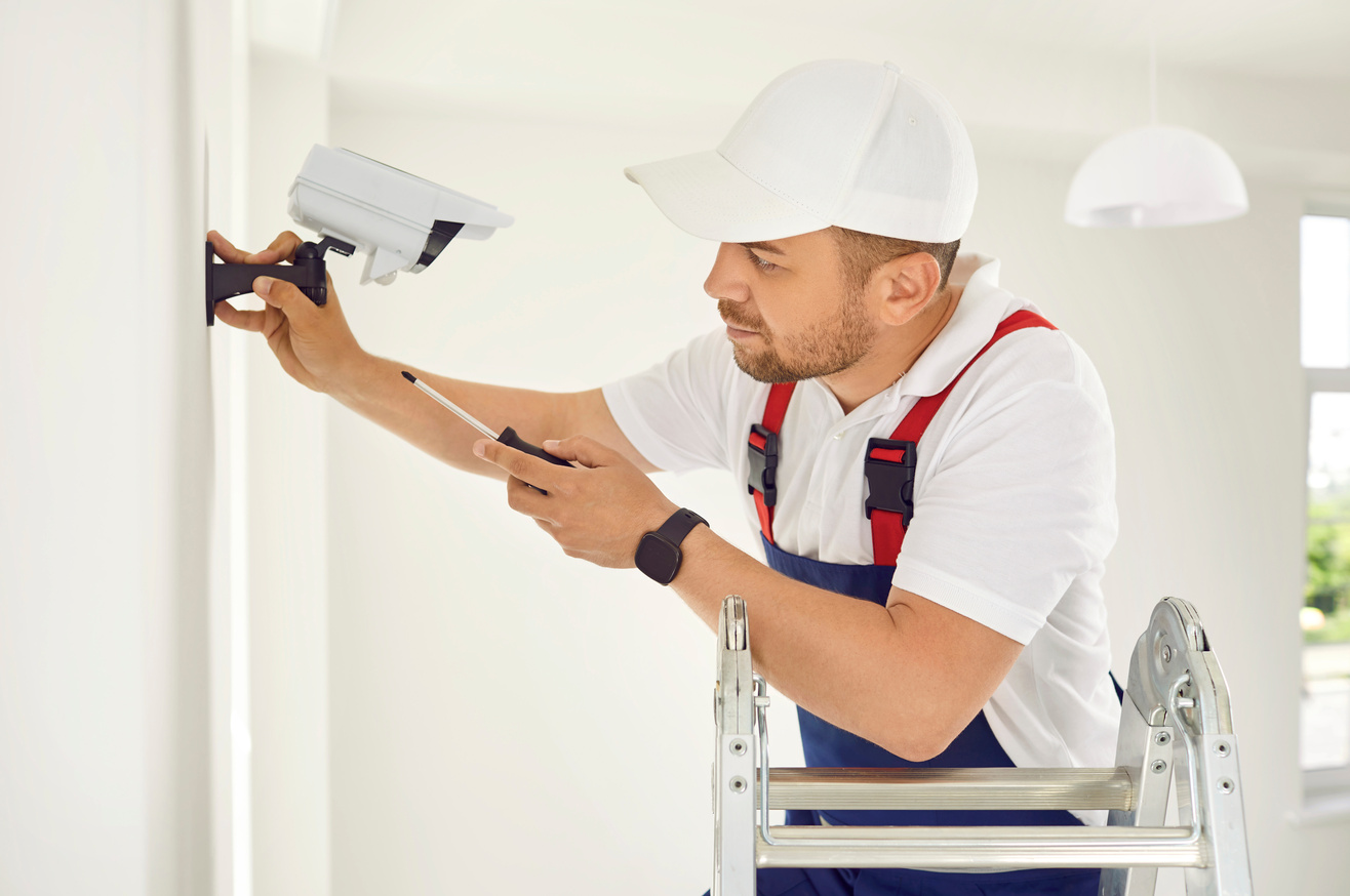 Electrician Worker Installs and Screws Surveillance Video Camera on Wall in Bright Office Space.